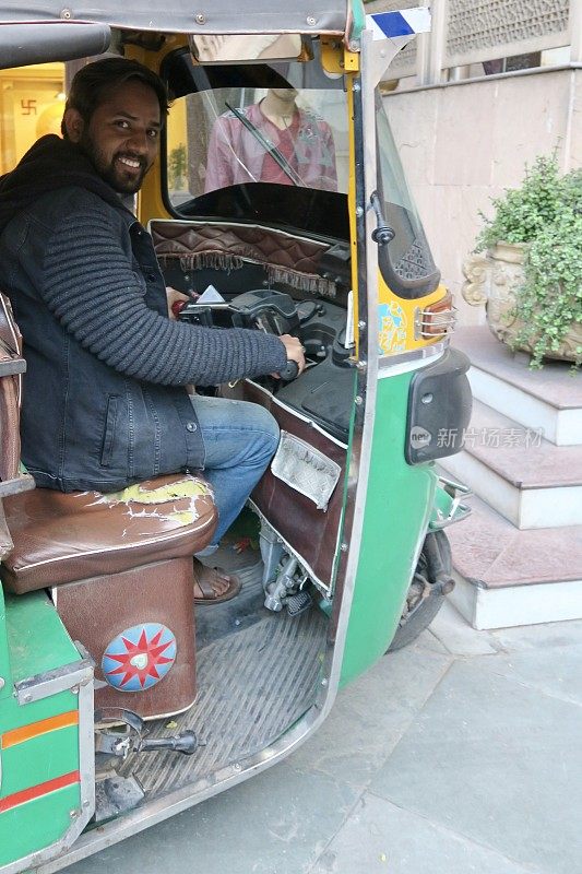 印度人驾驶机动三轮车/绿色和黄色嘟嘟车出租车司机在印度北部新德里的照片